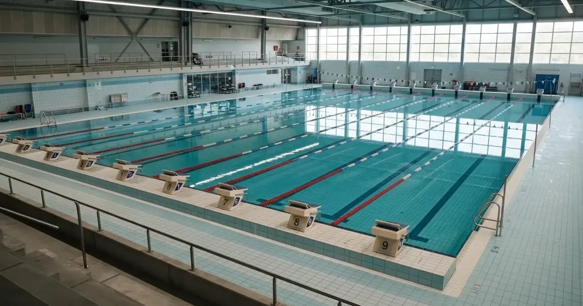 Pusty basen olimpijski z równymi torami i spokojną taflą wody, widok z trybun w jasnym świetle.
